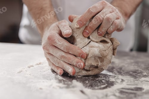 Preview: Professional baker kneads dough on the table in the kitchen of the bakery