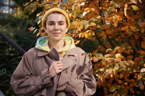 Preview: Young pleasant woman stands against the background of autumn tree