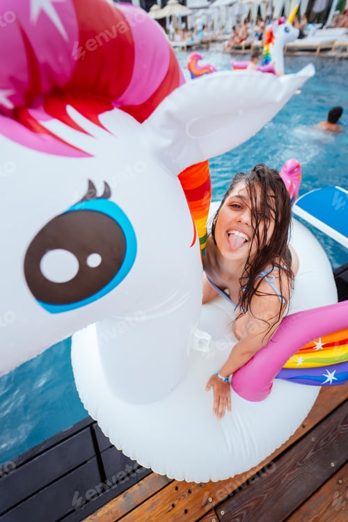 Preview: Happy young woman sitting on inflatable unicorn toy mattress