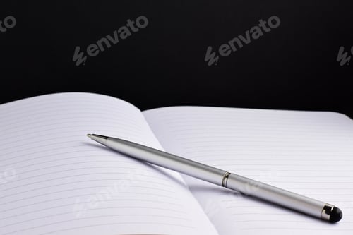 Preview: Metal pen on a notebook with a black background as an indication to good work ethic
