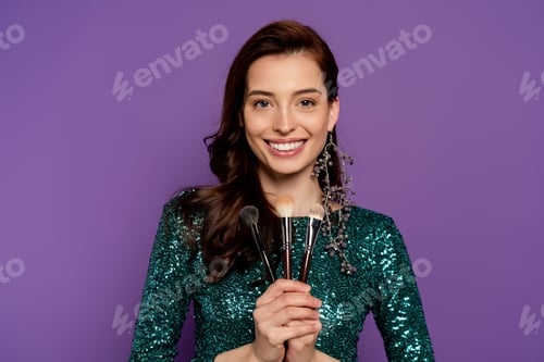 Preview: happy woman holding cosmetic brushes isolated on purple