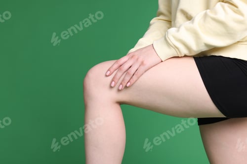 Preview: Young woman suffering from pain in knee on green background, closeup. Space for text