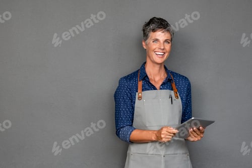 Preview: Mature woman in apron holding digital tablet