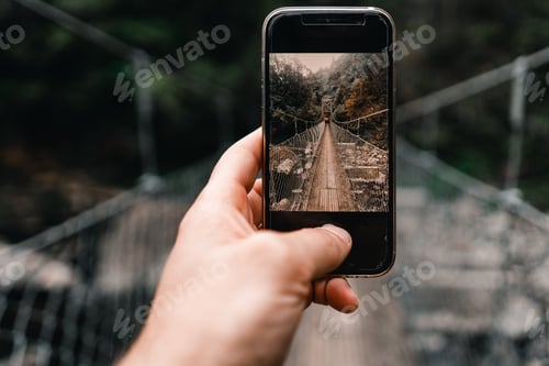 Preview: caucasian left hand holding a smartphone that on its screen shows a photograph of the long wooden