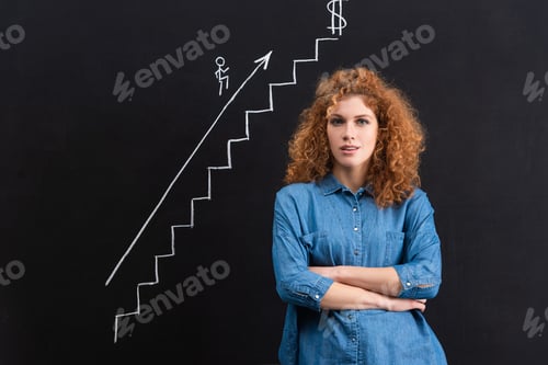 Preview: confident redhead girl with crossed arms, business growth on blackboard
