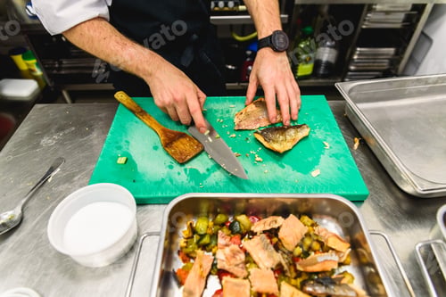 Preview: Kitchen of a restaurant with a cook placing fish in trays to roast it.