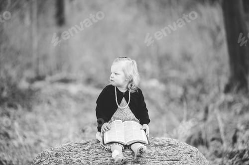 Preview: Greyscale shot of a little blonde girl sitting on a rock and holding a book