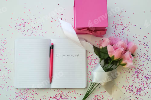 Preview: Open journal with proposal , pink pencil, pink gift box and pink flowers.