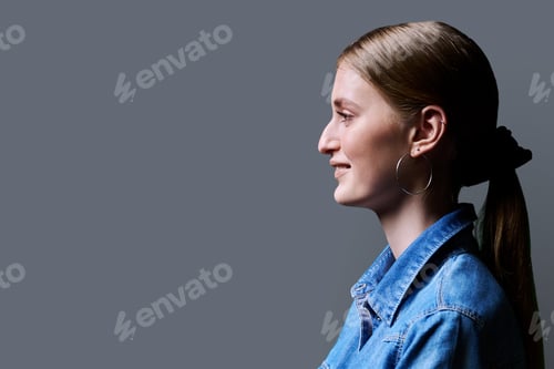 Preview: Profile view, young smiling female looking forward on gray studio background