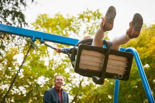Preview: Father pushing daughter on playground swing