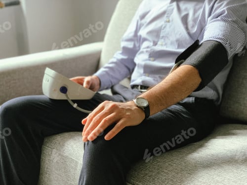 Preview: Man checking blood pressure at home. Sitting on sofa. Seasonal health issues or stress at work