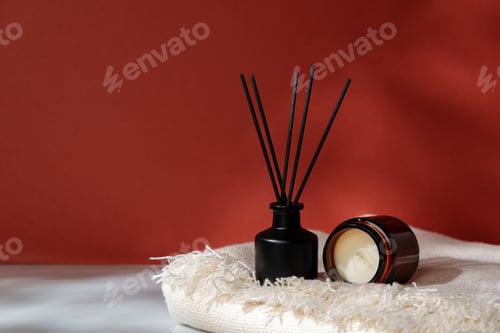 Preview: Aromatic Reed Diffuser and Scented Candle on a Woven Mat Against a Warm Red Background