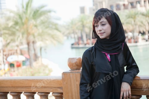 Preview: A woman in a hijab standing by a balustrade with a serene waterway in the background