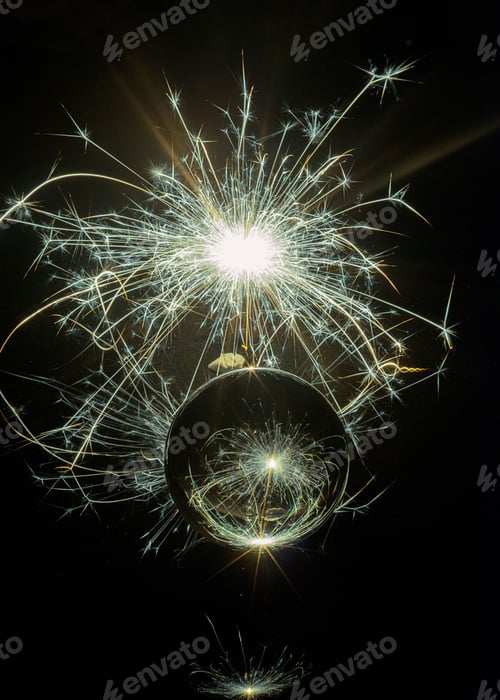 Preview: Vertical shot of a reflective glass ball in front of exploding colorful fireworks