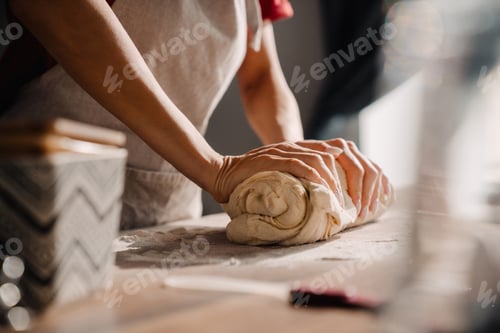 Preview: Young woman wearing apron cooking and kneading dough in kitchen