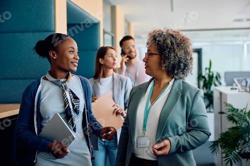 Preview: Happy black businesswoman talking to mature female CEO while walking through the office.