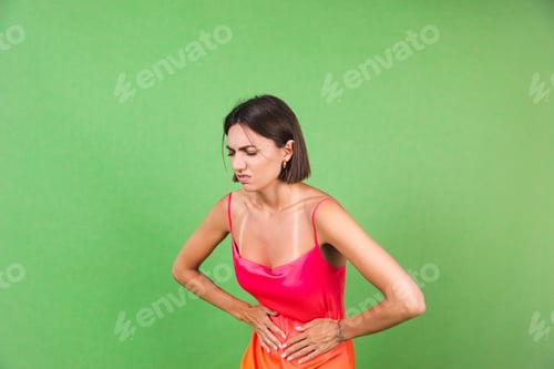 Preview: Stylish woman in pink silk dress isolated on green background suffering from stomach pain