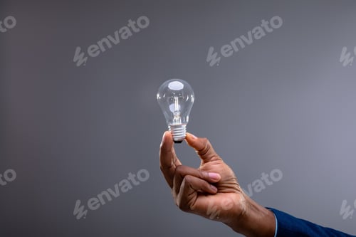 Preview: Close up of businessman holding light bulb against grey background