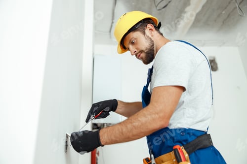 Preview: Male worker professional electrician in uniform installing electrical outlet in apartment after