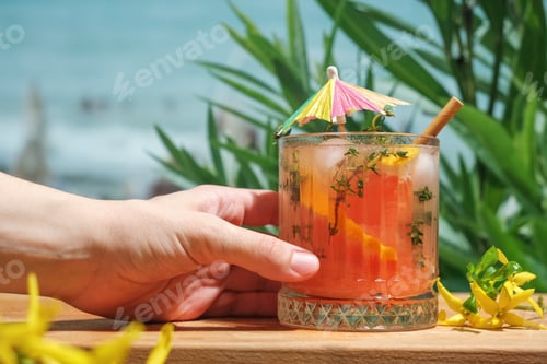 Preview: Hand holds glass of summer cocktail at beach bar