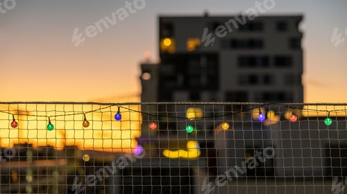 Preview: Net fence with festive multicolored string lights draped across it in the evening