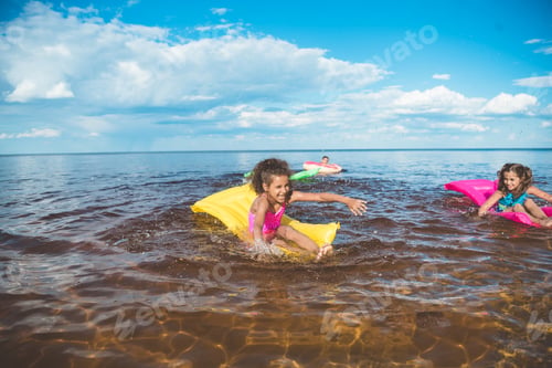Preview: multicultural little girls swimming on inflatable mattresses at sea together