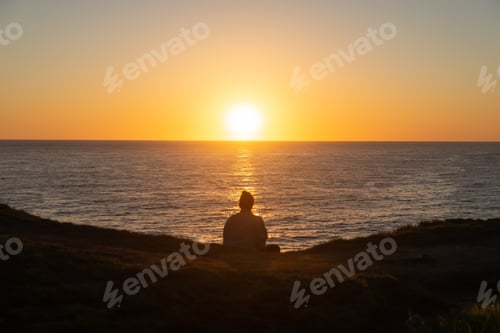 Preview: Rear View of Woman Silhouette Sitting in the Edge of a Hill Watching the Sunrise