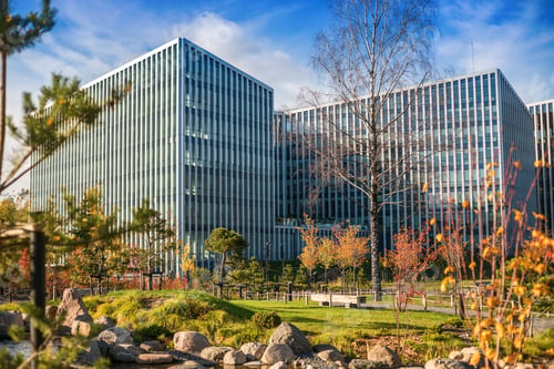 Preview: A sleek glass building reflects the sky and clouds, framed by grass, autumn trees, and a pond