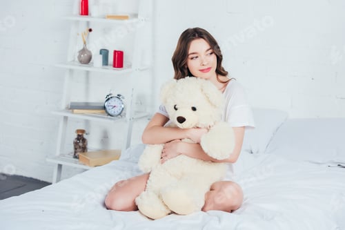 Preview: beautiful woman hugging teddy bear and sitting on bed with white bedding