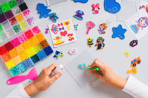 Preview: Children's hands put aqua beads on the board and a set for making top view