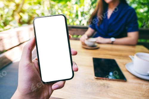 Preview: A man holding black mobile phone with blank white screen with woman drinking coffee in cafe