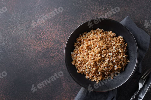 Preview: Wholegrain spelt farro in bowl on brown background. Top view.