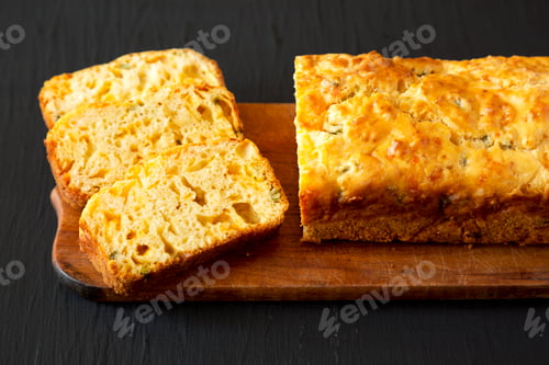 Preview: Homemade Cheesy Bread Loaf on a rustic wooden board on a black surface, side view.