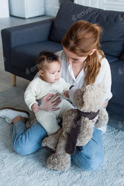 Preview: woman sitting on floor with african american baby girl and teddy bear