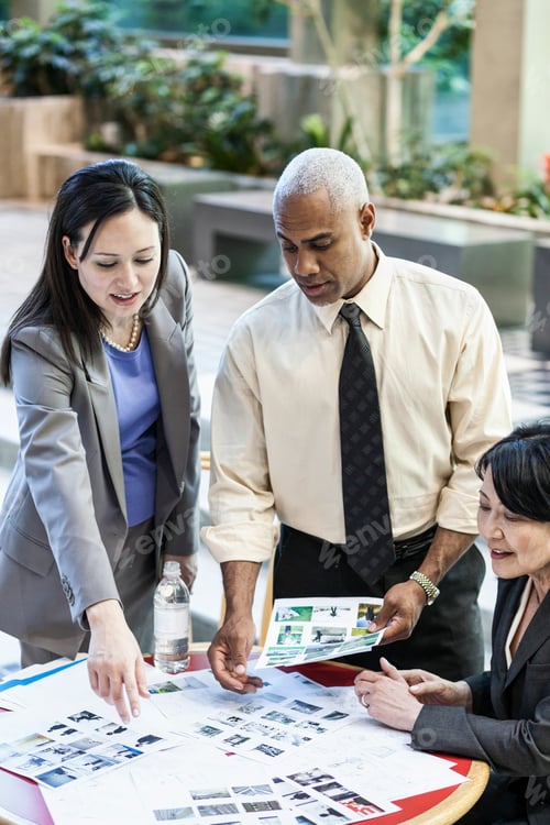Preview: Mixed race group of three people in an informal meeting around a table in a lobby area.