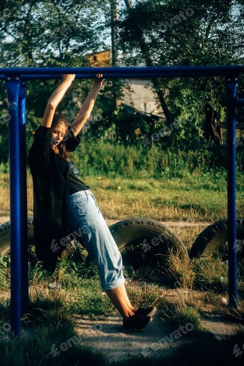 Preview: Fashionable cool woman playing and hanging on horizontal bars in evening