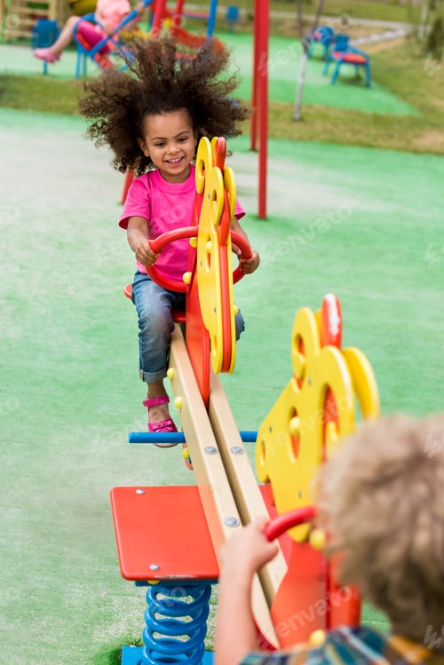 Preview: happy curly african american child riding on rocking horse with boy at playground