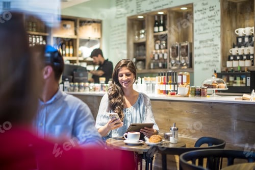 Preview: Young woman with digital tablet reading smartphone texts in cafe