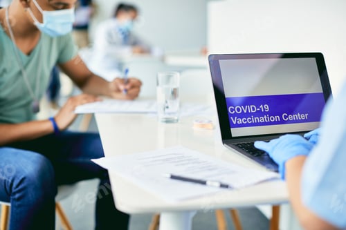 Preview: Close-up of healthcare worker working on laptop at COVID-19 vaccination center.