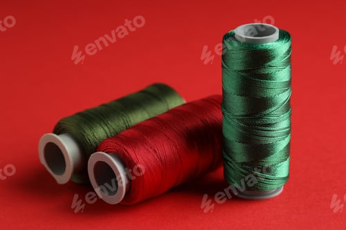 Preview: Different spools of sewing threads on red background, closeup