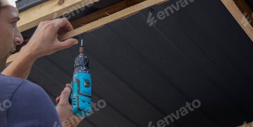 Preview: a man repairs the roof, tightens the self-tapping screw with a screwdriver.