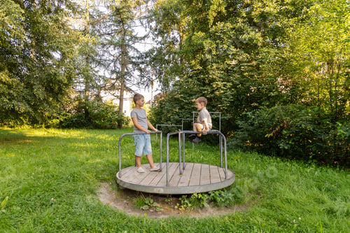 Preview: Two children are having fun on a merry-go-round in a lush park.