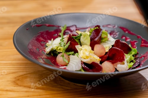 Preview: close-up on black plate with lettuce leaves beet slices and round pieces of apple