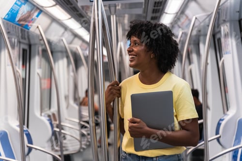 Preview: Smiling woman standing with laptop in subway train