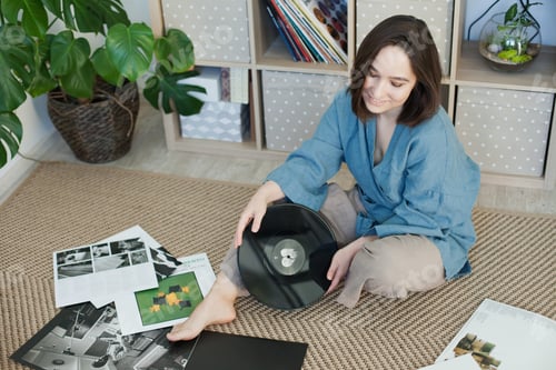 Preview: Young woman sitting on the rug at home with records listening to music, relaxing moments