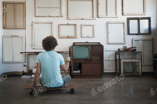 Preview: A man sitting on a skateboard looking at a wall of reversed picture frames.