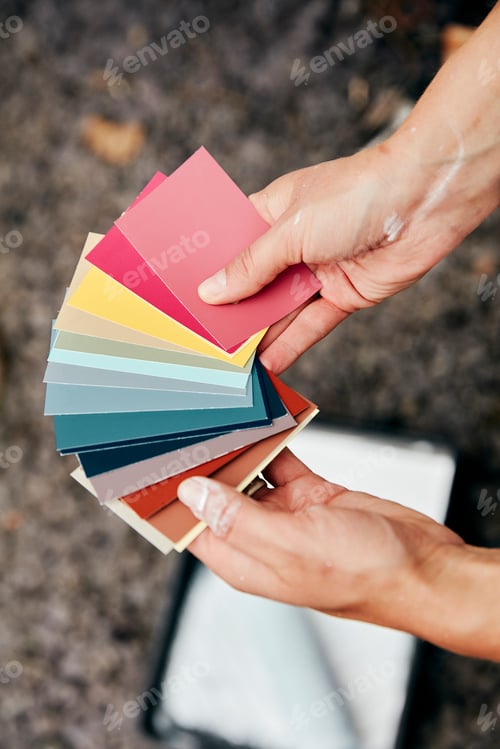 Preview: A person holding a paint colour chart, and a paint tray and roller in the background.