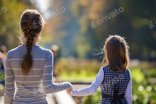 Preview: Back view of child girl and mother in dresses together holding hands on warm day