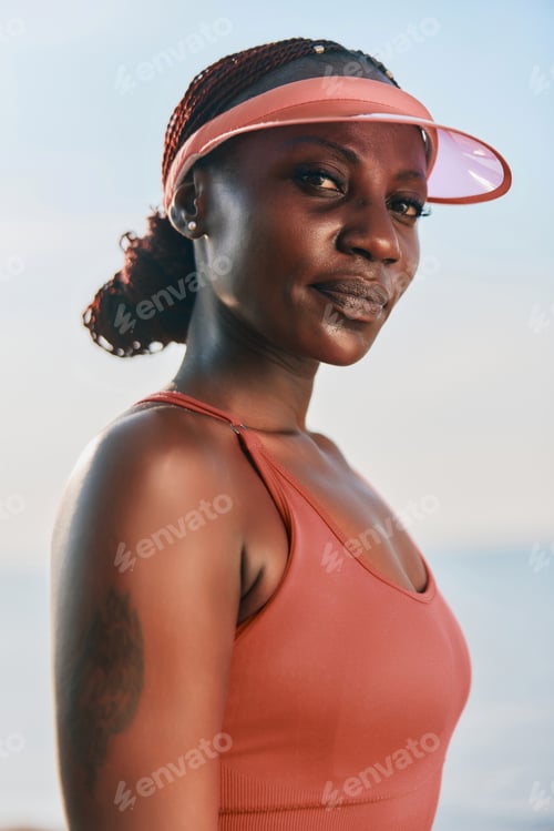 Preview: Confident woman in athletic wear with a visor, standing by the water, showcasing strength and