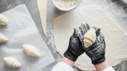 Preview: Baker showing freshly made croissant in hands wearing black gloves